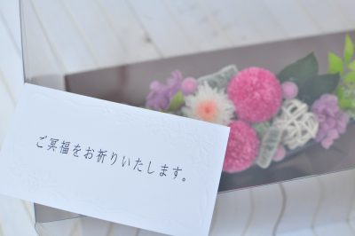 ピンクと白の花びらの花でお供え用にアレンジした花と、ご冥福をお祈りしますのカードの写真