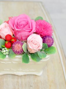 白い器にピンクのバラと赤い実が入ったアレンジメント
