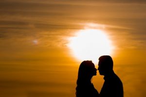 夕日をバックにカップルがキスしそうな距離で見つめあっている