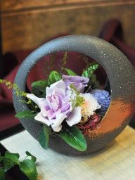 黒い和風な器に紫のクチナシやバラ、淡いピンクの小菊などをアレンジしたプリザーブドフラワー