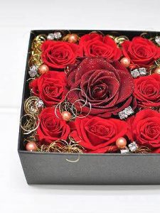 黒い正方形のボックスの中央にダイヤモンドの粒子が散りばめられた大輪の赤いバラが1輪あり周りには8輪の赤いバラとパールなどが敷き詰められている