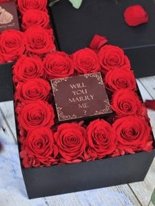 黒い正方形のボックスの中央には【WILL YOU MARRY ME?】と書かれたプレートがありその周りには赤い12輪のバラとアジサイが敷き詰められている
