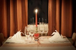 レストランの窓際のような場所にセットされたテーブルコーディネート。テーブルの真ん中には赤いキャンドルが1本立っていて窓からは夜景が見えるロマンティックな空間