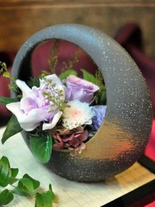 黒色の円盤型の器に紫色の花などを使ったアレジメント