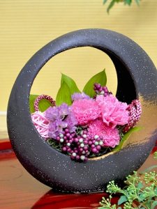 黒色の丸い器にピンクと紫の花のアレジメント